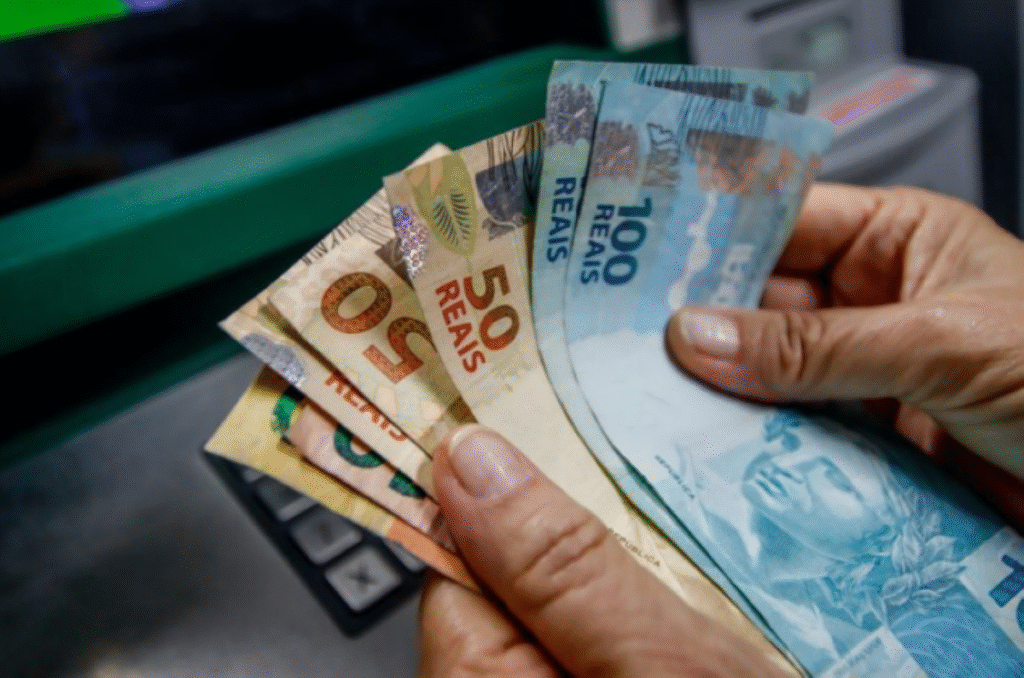 Pessoa segurando cédulas de reais em frente a caixa eletrônico.