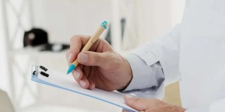 Mão segurando uma caneta e anotando em um bloco de notas, simbolizando inspeção médica ou exames de saúde.