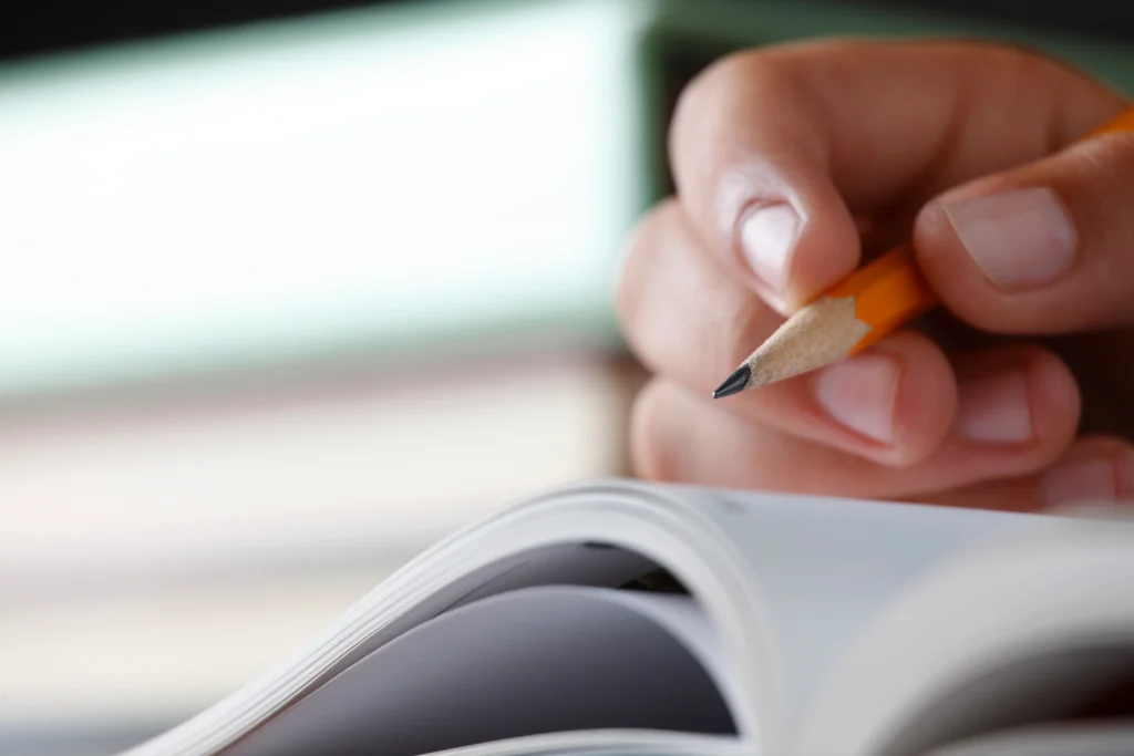 Pessoa segurando lápis enquanto preenche inscrição em caderno, representando etapa de inscrição no concurso da Prefeitura de Santa Cruz do Sul.
