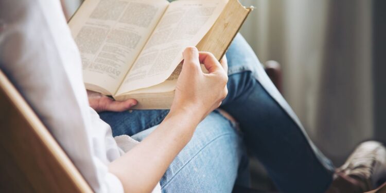 Pessoa lendo um livro com as mãos em uma poltrona confortável, representando a importância de leituras relaxantes e obras literárias alternativas para concurseiros recarregarem as energias e manterem a mente ativa durante a preparação.