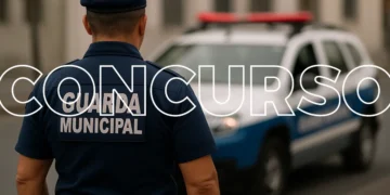 Fotografia de um guarda municipal de costas, usando uniforme azul-marinho e boina preta, com a viatura da Guarda Municipal desfocada ao fundo.
