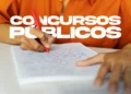 Pessoa escrevendo com caneta vermelha em caderno, preparação para concursos públicos.