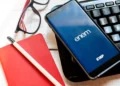 Smartphone com tela do aplicativo ENEM ao lado de caderno vermelho, óculos e teclado de computador
