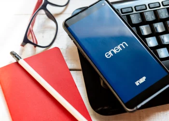 Imagem de materiais de estudo para o Enem 2025, incluindo um smartphone com o logo do Enem, caderno, caneta e óculos, representando a preparação para a prova.