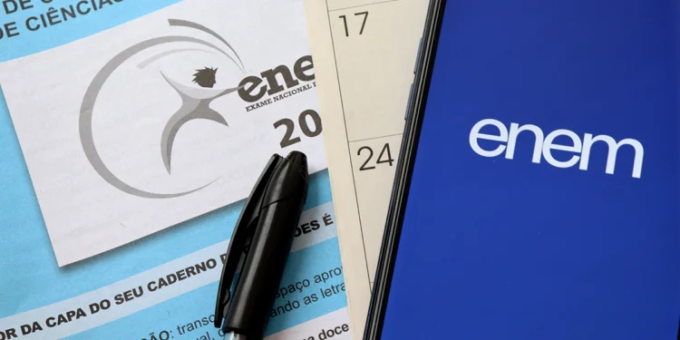 Caderno do ENEM, caneta preta e telefone celular com logo do ENEM sobre calendário com datas destacadas.