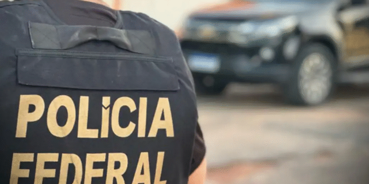 Agente da Polícia Federal com colete e viatura ao fundo.