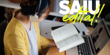 Mulher jovem estudando com fones de ouvido, anotando em caderno e usando laptop em ambiente de estudo.