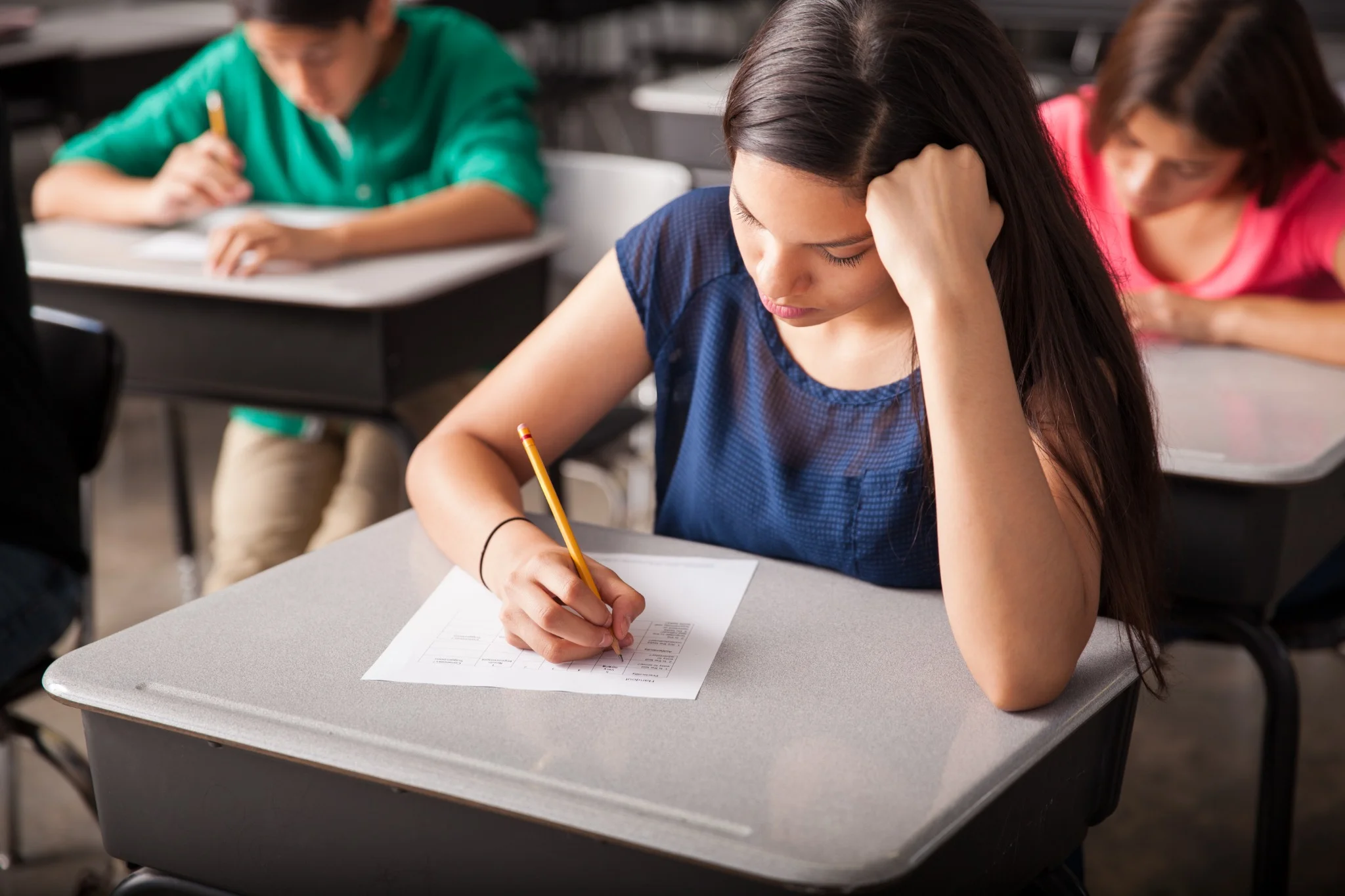 Estudantes realizando um teste em sala de aula, com foco em uma aluna que está preenchendo um formulário, representando a preparação para a Prova Nacional Docente (PND) 2025