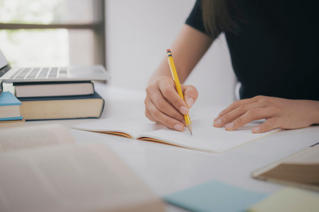 Pessoa escrevendo em um caderno, representando preparação para concurso público de médicos no GRAU-SP.