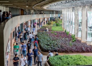 Estudantes circulando pelo campus de uma universidade federal brasileira, com área verde e estrutura arquitetônica moderna.
