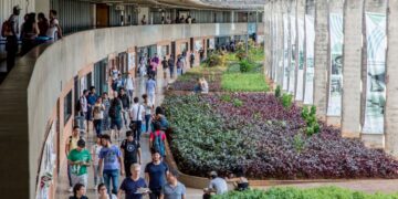 Estudantes circulando pelo campus de uma universidade federal brasileira, com área verde e estrutura arquitetônica moderna.