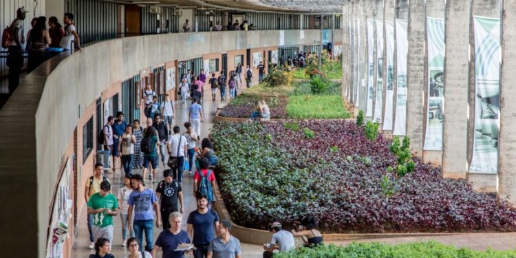 Estudantes circulando pelo campus de uma universidade federal brasileira, com área verde e estrutura arquitetônica moderna.