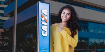 Mulher com suéter amarelo apontando para letreiro azul com logo da Caixa Econômica Federal em prédio comercial