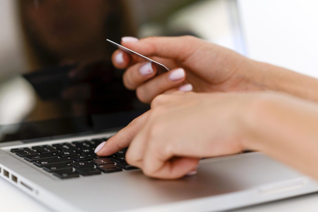 Mãos femininas digitando no teclado do notebook enquanto seguram cartão de crédito para compras online