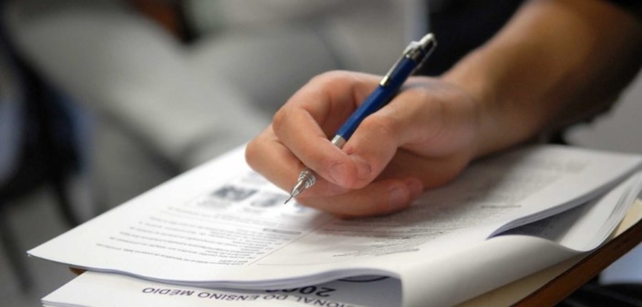 Candidato realizando prova do Encceja. Pessoa preenchendo prova impressa com caneta, representando candidatos aguardando o resultado do Encceja.