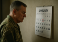 Homem em uniforme militar olhando atentamente para calendário com dia 12 de janeiro destacado em vermelho