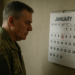 Homem em uniforme militar olhando atentamente para calendário com dia 12 de janeiro destacado em vermelho