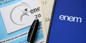 Caderno de prova do Enem com caneta preta e calendário ao lado de celular com logo do Enem na tela.