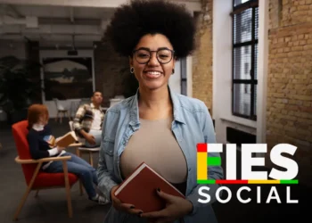 Jovem sorridente segurando livro, com logo FIES Social, sala de estudo ao fundo.