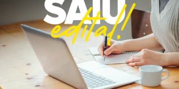 Pessoa fazendo anotações ao lado de notebook, com texto "Saiu edital!" destacado.