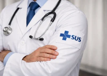 Profissional de saúde do SUS com jaleco branco e estetoscópio, símbolo do SUS visível.