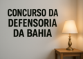 Parede com a frase 'Concurso da Defensoria da Bahia' e um abajur aceso sobre uma mesa