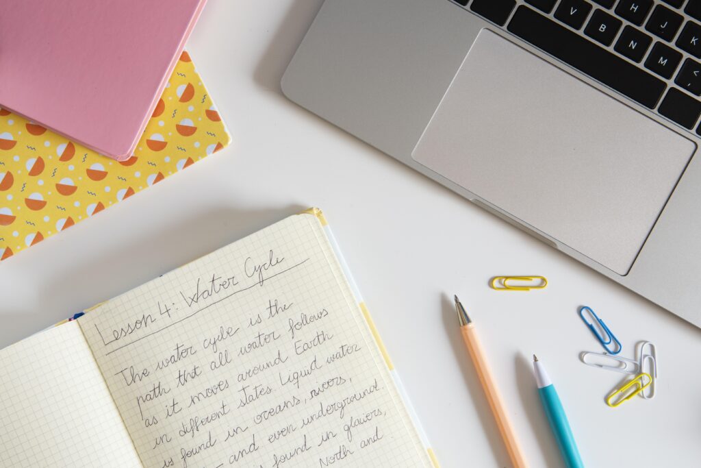 Materiais de estudo e anotação sobre grafia correta de descansar ou descançar Caderno aberto, canetas, clipes coloridos e parte de notebook sobre mesa, destacando tema palavras que confundem