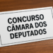 Placa escrita 'Concurso Câmara dos Deputados' sobre mesa de madeira.