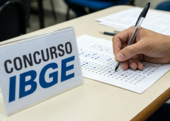 Candidato preenche cartão-resposta com caneta ao lado de placa do concurso IBGE