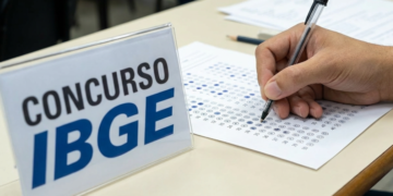 Candidato preenche cartão-resposta com caneta ao lado de placa do concurso IBGE