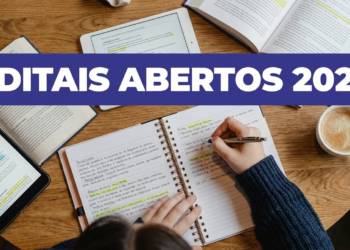 Pessoa escrevendo em caderno ao lado de livros, tablet e xícara de café