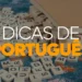 Peças de madeira de um jogo de palavras espalhadas sobre uma mesa azul, com um livro aberto ao lado e o texto "Dicas de Português" sobreposto.