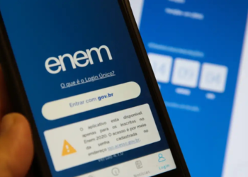 Mão segurando celular com tela do Enem aberta exibindo opção de login e aviso importante