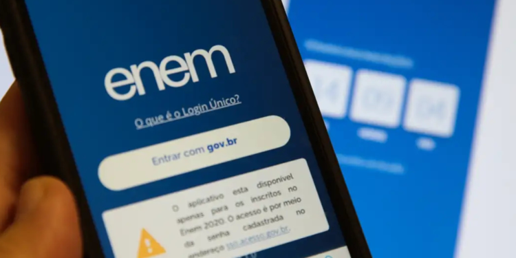 Mão segurando celular com tela do Enem aberta exibindo opção de login e aviso importante