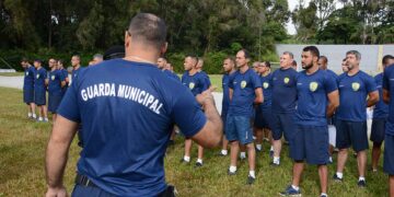 Instrutor aponta para grupo de candidatos da Guarda Municipal em formação ao ar livre