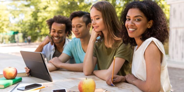 Jovens sorrindo e atentos ao notebook encima da mesa.