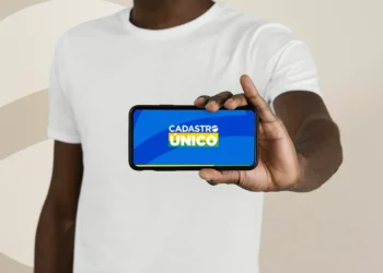 Homem negro de camiseta branca segura smartphone horizontal com tela do aplicativo Cadastro Único para Programas Sociais do Governo Federal