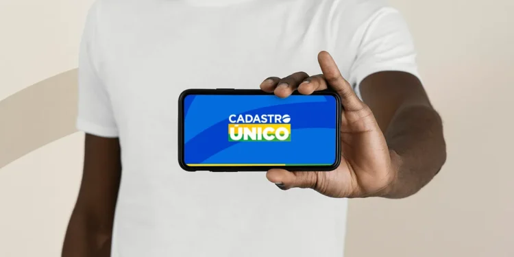 Homem negro de camiseta branca segura smartphone horizontal com tela do aplicativo Cadastro Único para Programas Sociais do Governo Federal