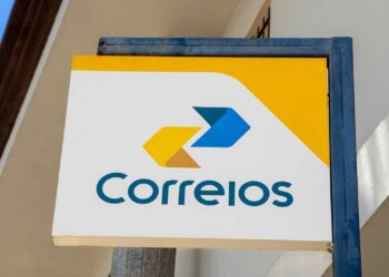 Placa retangular dos Correios com logotipo amarelo e azul e fundo branco em fachada externa