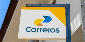 Placa retangular dos Correios com logotipo amarelo e azul e fundo branco em fachada externa