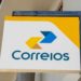Placa retangular dos Correios com logotipo amarelo e azul e fundo branco em fachada externa