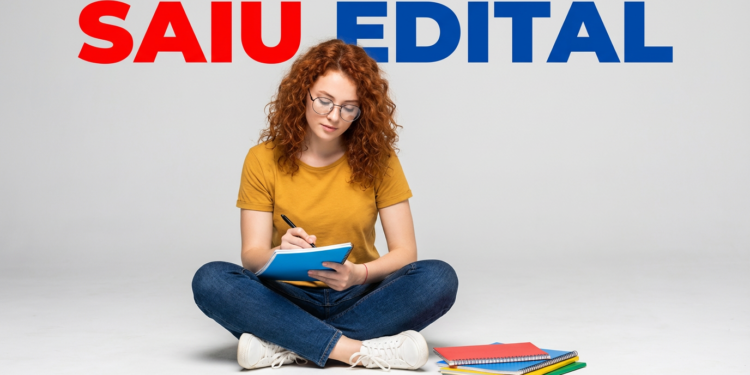 Jovem ruiva de óculos sentada no chão escrevendo em caderno azul com texto "Saiu Edital" ao fundo