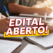 Mãos de pessoas escrevendo em cadernos com canetas sobre mesa de madeira e texto "EDITAL ABERTO!" em destaque