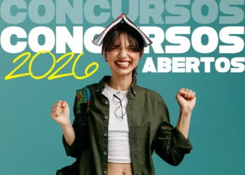 Jovem sorridente com livro aberto na cabeça, jaqueta verde e óculos pendurados, celebrando concursos 2026