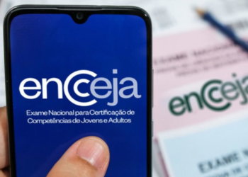 Tela de celular com logo do Encceja e prova impressa ao fundo sobre mesa