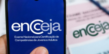 Tela de celular com logo do Encceja e prova impressa ao fundo sobre mesa