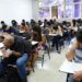 Candidatos realizando prova em sala de aula com carteiras escolares