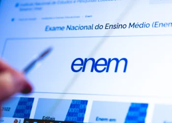 Tela do site do ENEM com logo azul, texto "Exame Nacional do Ensino Médio" e mão apontando caneta para o monitor