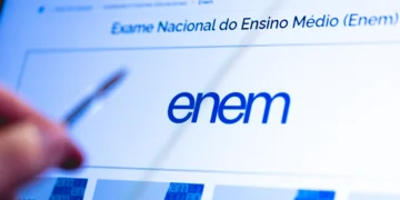 Tela do site do ENEM com logo azul, texto "Exame Nacional do Ensino Médio" e mão apontando caneta para o monitor