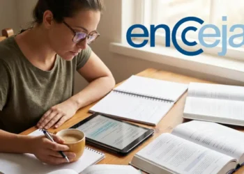 Mulher de óculos estuda com tablet, caderno e livros abertos em mesa com logo ENCCEJA visível